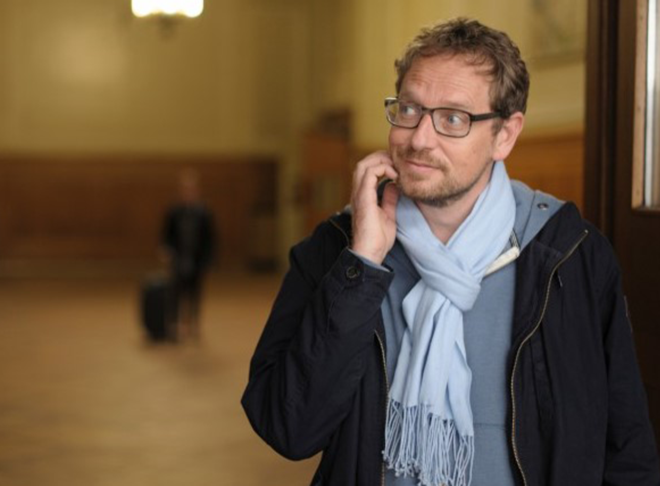 A man in glasses with scarf and coat.